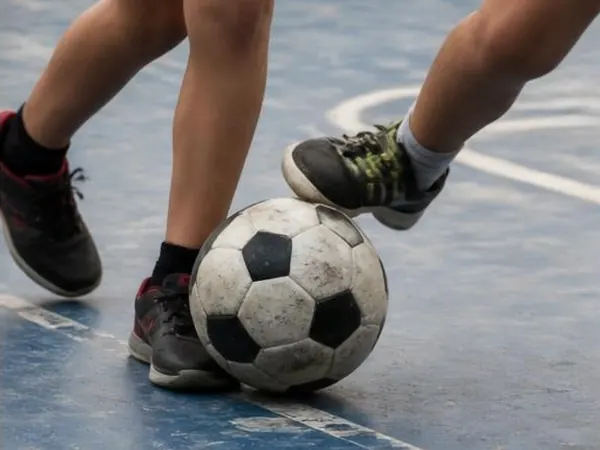 Piernas de chicos con zapatillas pateando una pelota en una cancha de futsal de barrio